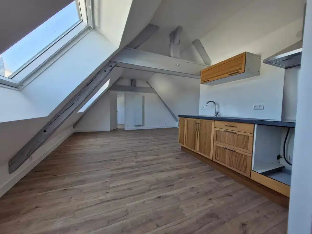 Cuisine aménagée sous combles avec meubles bois, plan de travail noir et fenêtre de toit