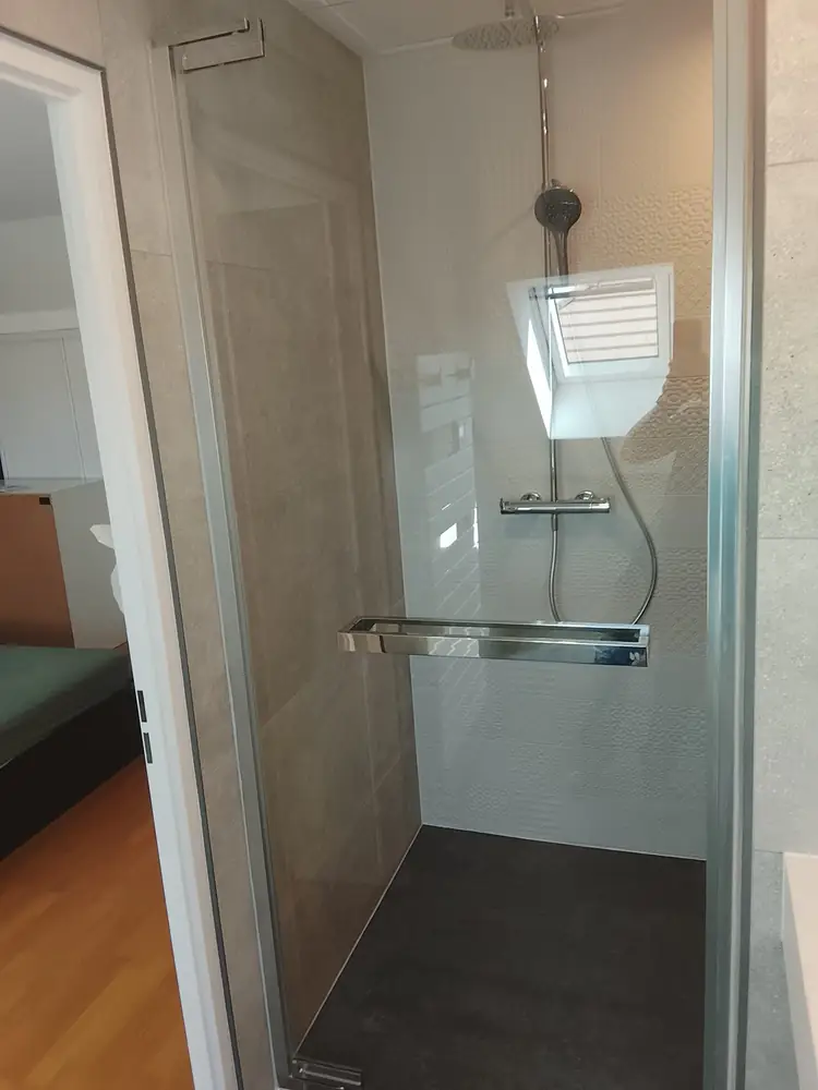 Douche avec paroi vitrée, colonne de douche thermostatique et faïence murale grise dans une salle d'eau rénovée