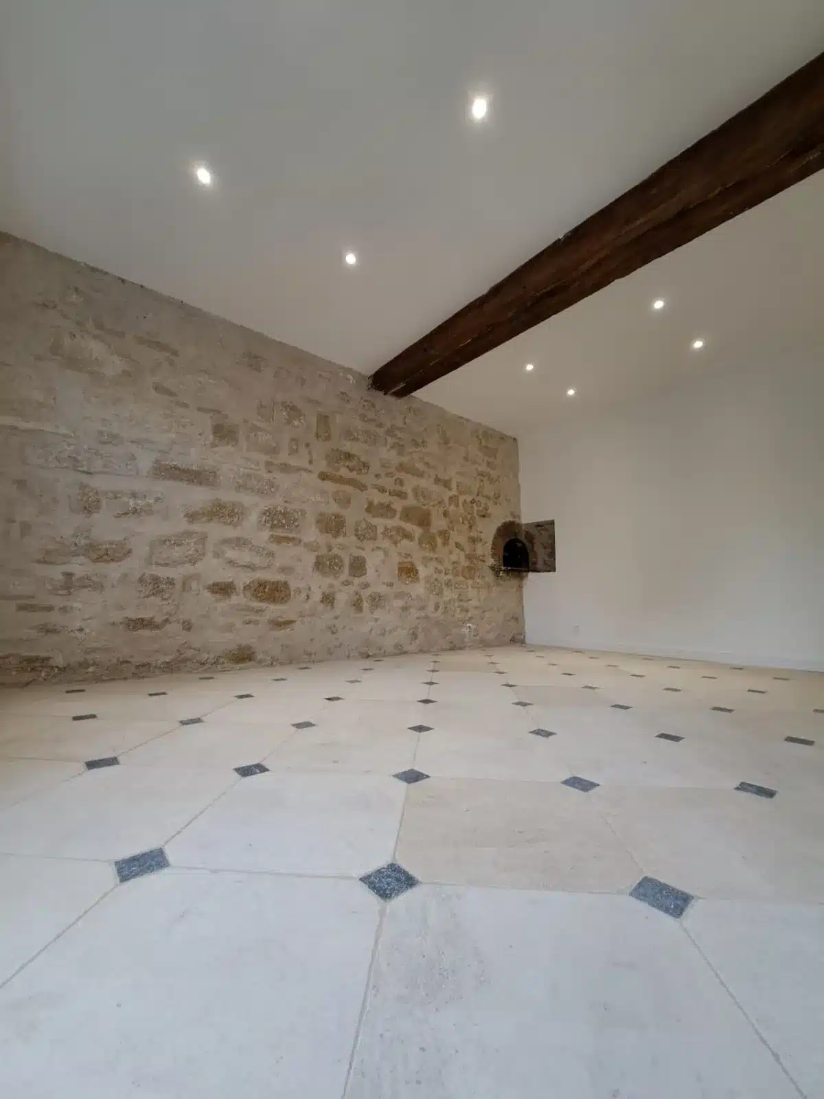 Pièce rénovée avec mur en pierre apparente, poutre, spots encastrés et carrelage à cabochons