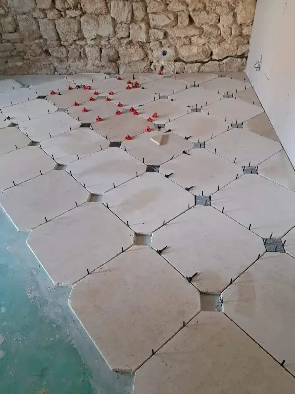 Pose de carrelage en pierre naturelle — ECP Rénovation Dalles de pierre claire en cours de pose avec croisillons rouges