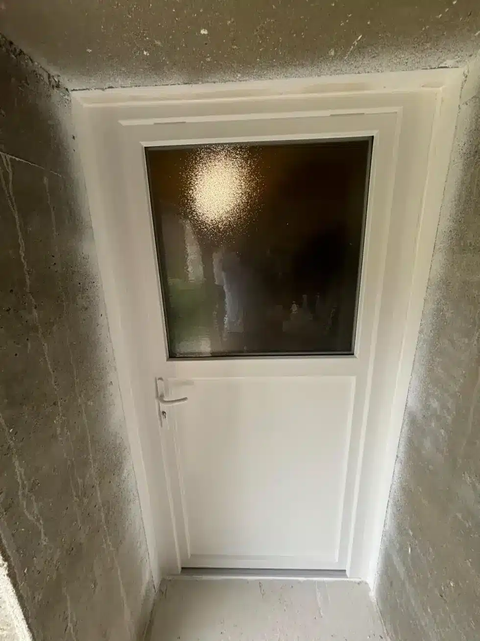 Porte d'entrée blanche neuve avec vitrage dépoli posée dans un encadrement rénové