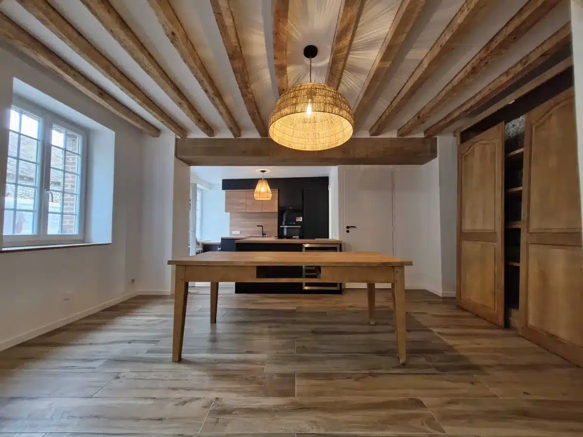 Cuisine ouverte sur la salle à manger avec poutres apparentes, table en bois et suspension en rotin
