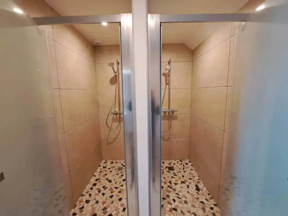Deux cabines de douche avec parois vitrées, faïence beige et sol en galets