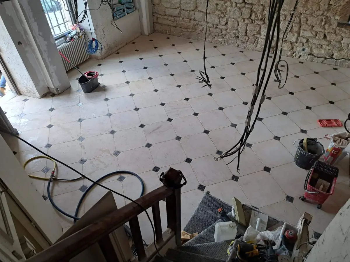 Rénovation intérieure : carrelage à cabochons — ECP Rénovation Sol en carrelage blanc à cabochons noirs posé dans une pièce en travaux aux murs en pierre