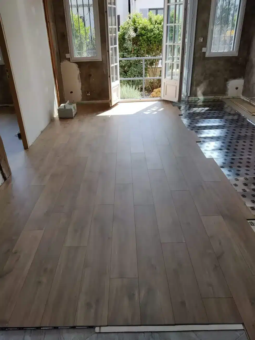 Rénovation intérieure, pose d'un sol — ECP Rénovation Pièce rénovée avec sol imitation bois foncé et portes-fenêtres