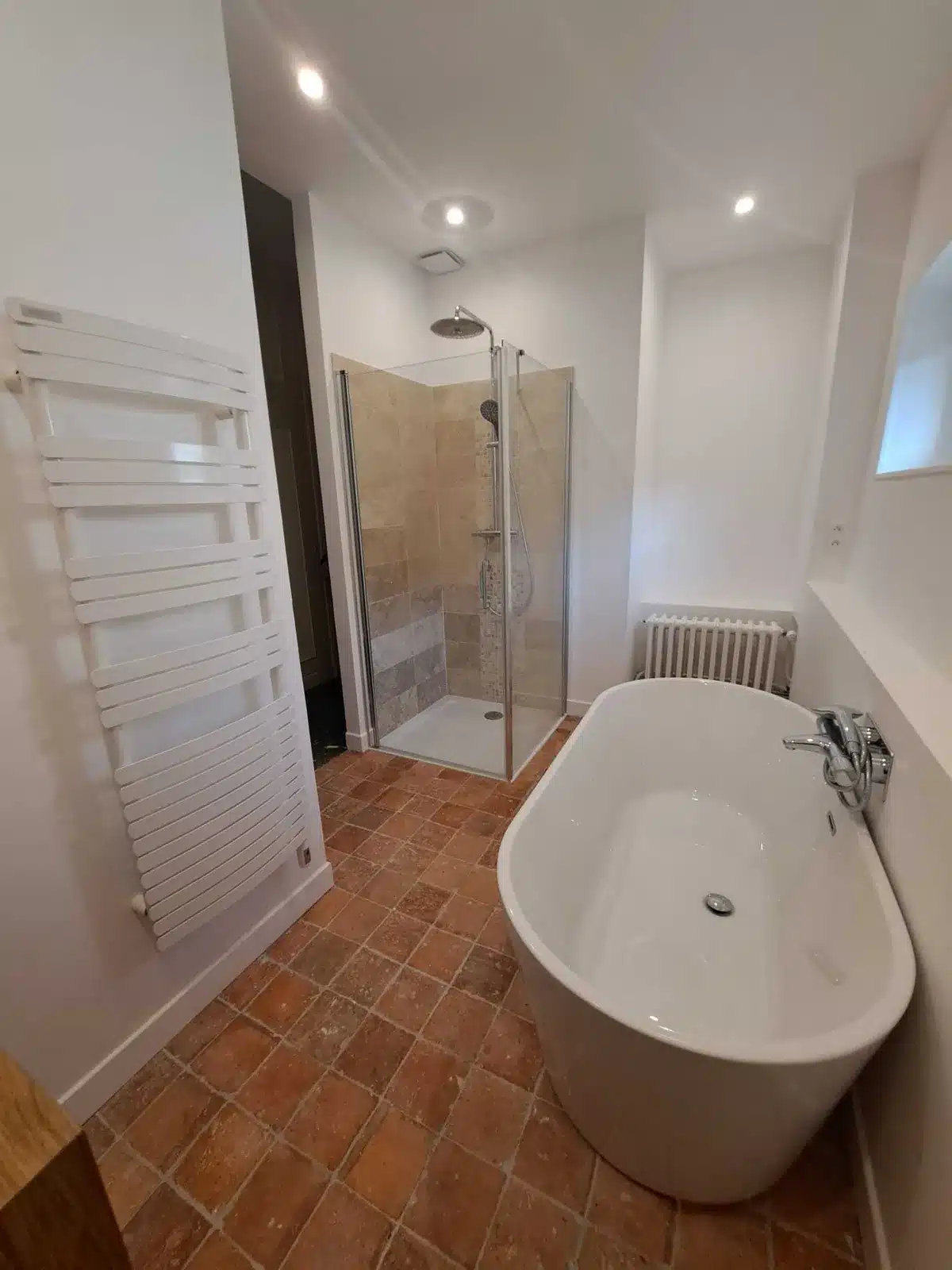 Salle de bain avec baignoire îlot, douche vitrée, sèche-serviettes et sol en tomettes
