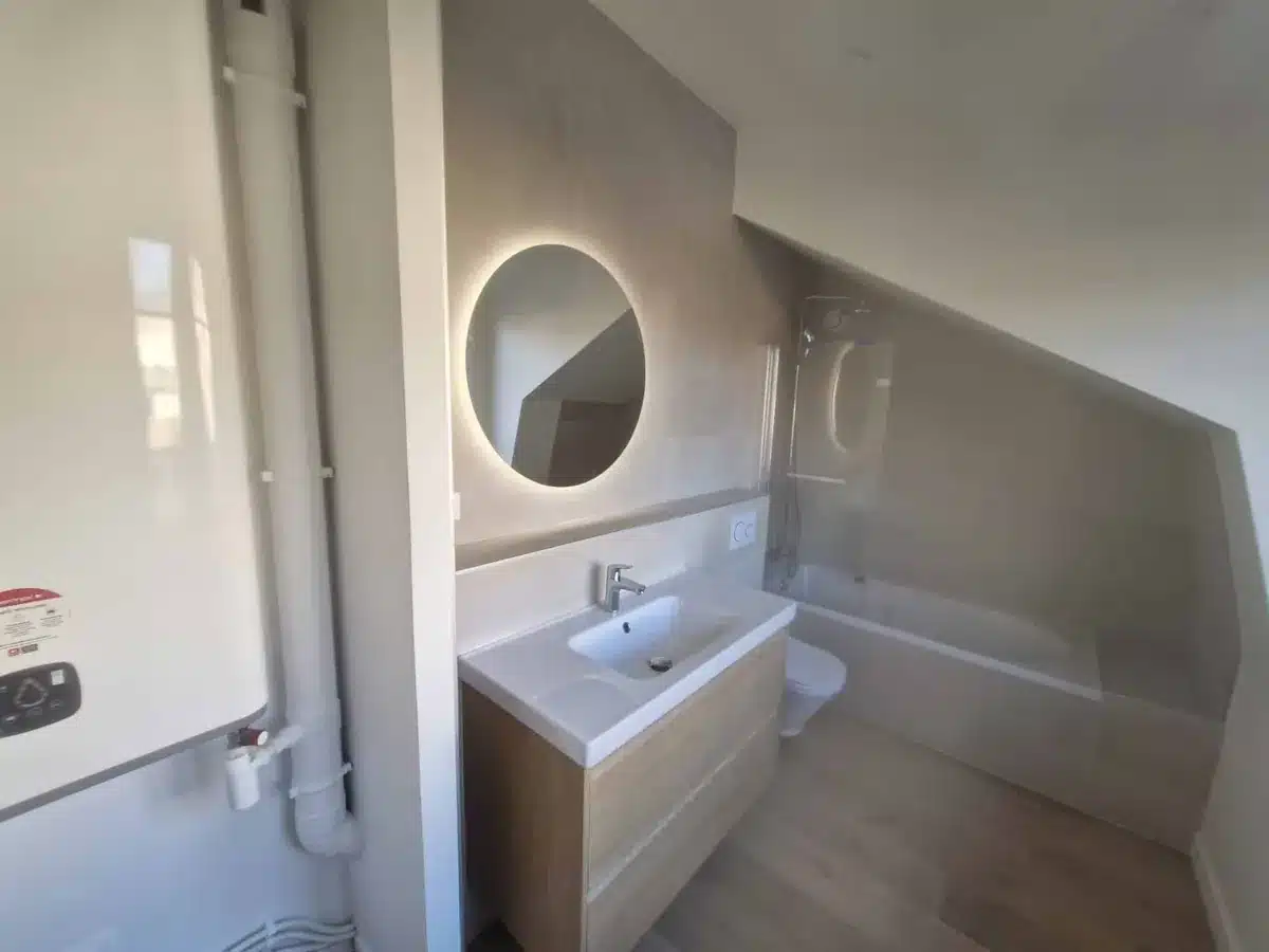 Petite salle de bain sous pente avec miroir rond lumineux, meuble vasque et douche