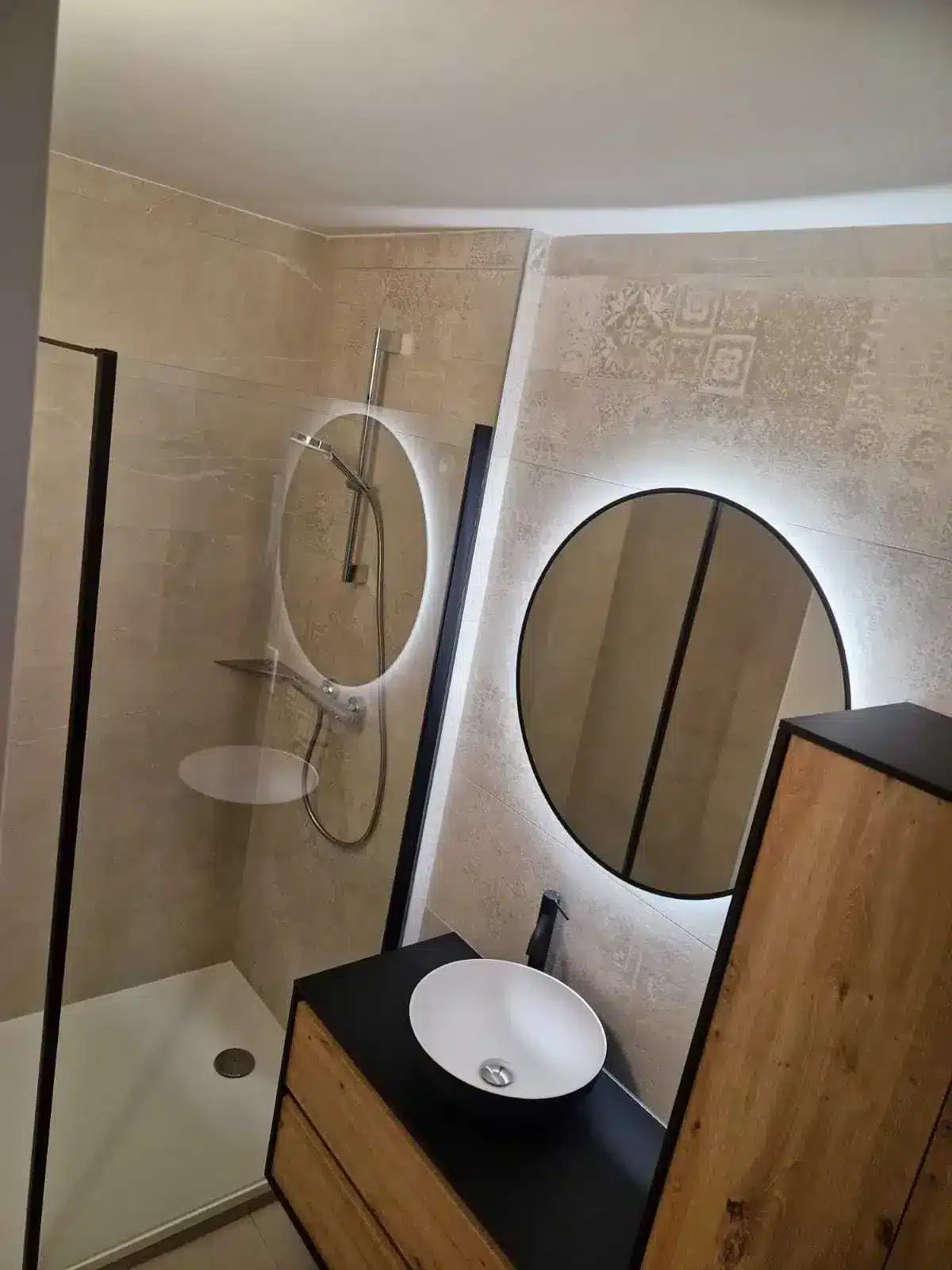 Salle de bain avec douche, miroir rond lumineux, vasque à poser et meuble noir et bois