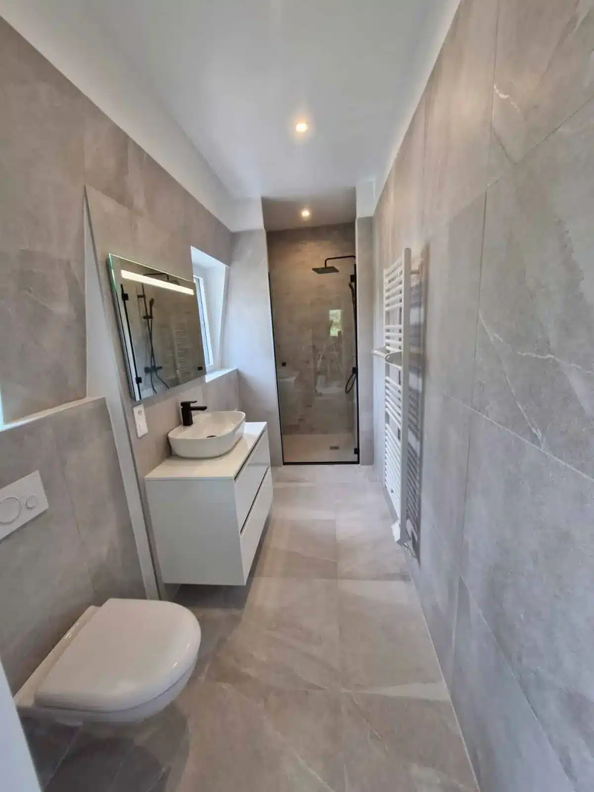 Salle de bain en longueur avec WC suspendu, vasque à poser, douche au fond et faïence grise