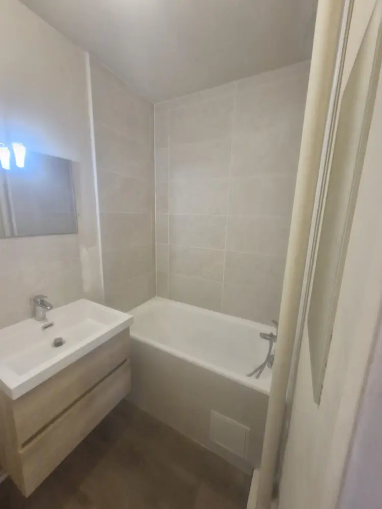 Vue de la baignoire et du lavabo avec faïence murale claire dans une salle de bains rénovée à Rambouillet