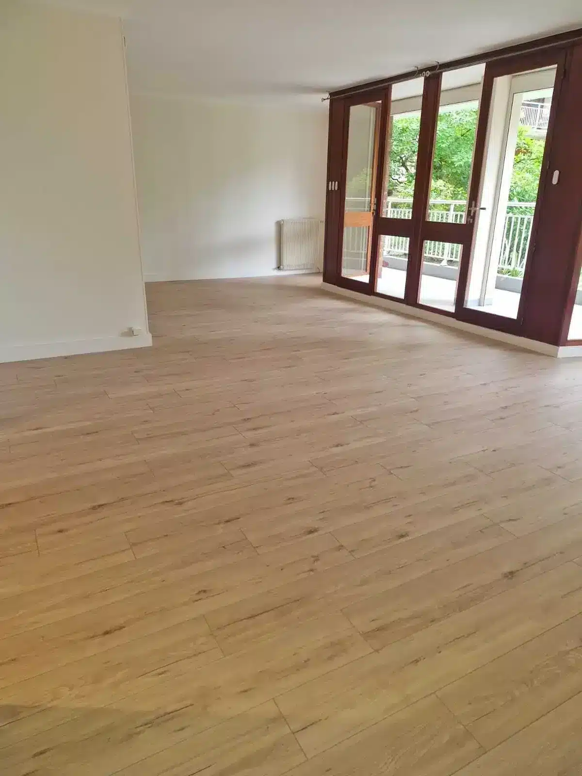 Séjour vide et lumineux avec parquet clair et baie vitrée donnant sur le jardin